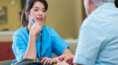 A person in blue scrubs talking to a person Description automatically generated